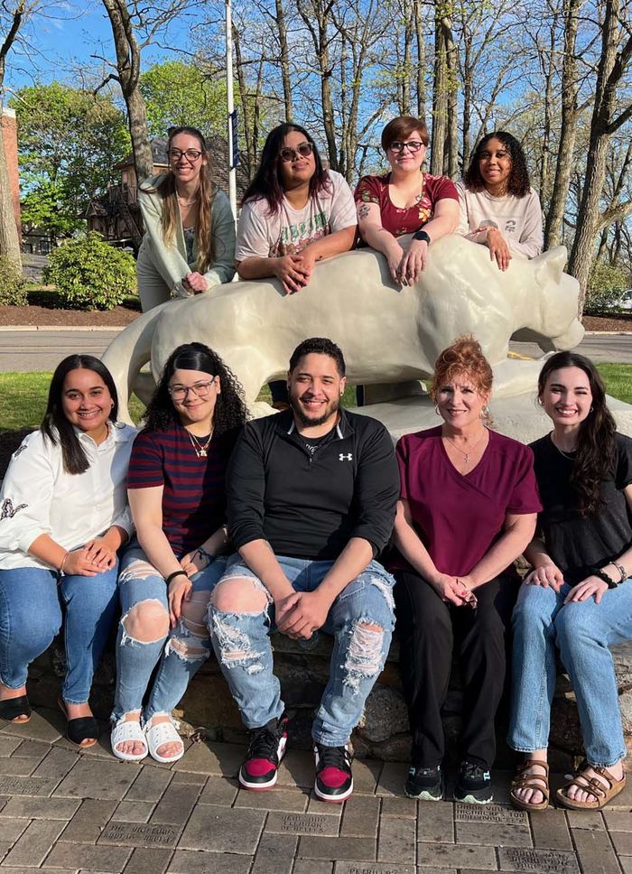Group of nine men and women seated outdoors around a nittany lion statue.