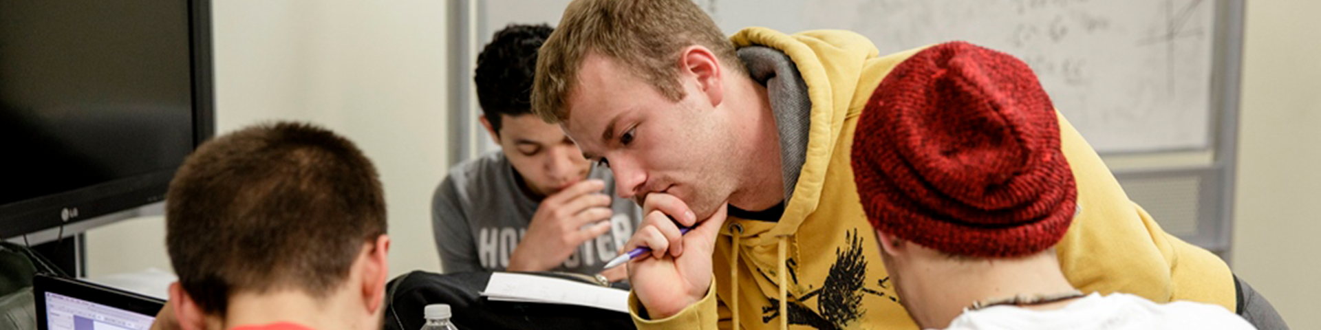 Male student in yellow hoodie looking at a paper.