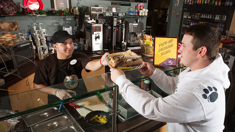 A student takes a sandwich from a student server at Higher Grounds.
