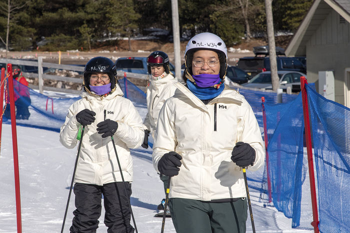 Students in white winter jackets skiing down a snow slope.