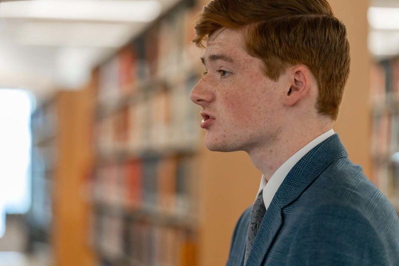 A male student speaks from a podium inside a library.