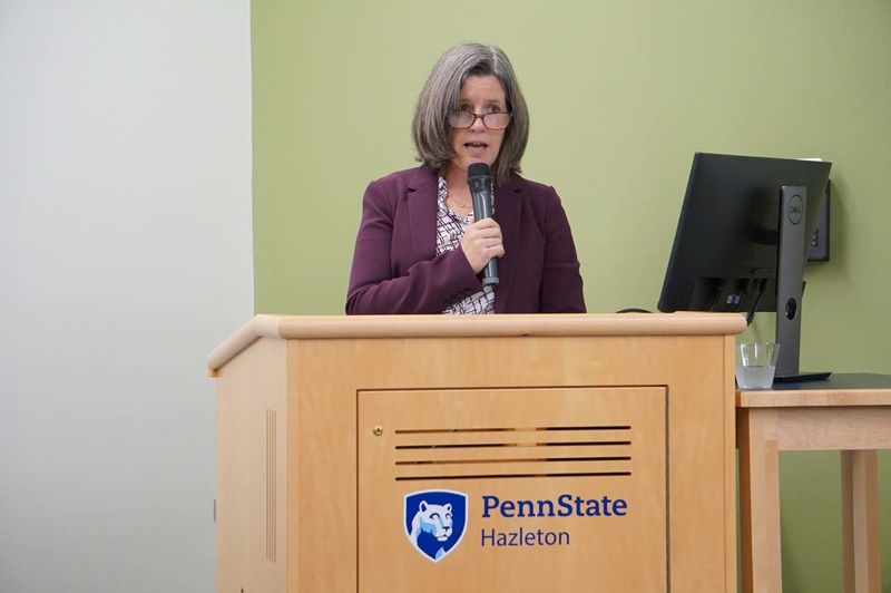 Woman holding microphone and speaking from behind a wooden podium with Penn State Hazleton mark on it.