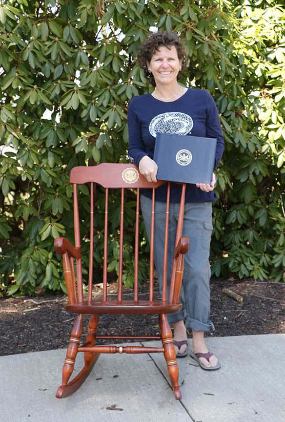 Woman standing in front of rocking chair holding a certificate.