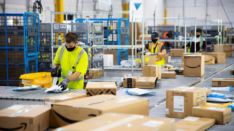 Amazon employees wearing masks sort numerous packages at a fulfillment center.