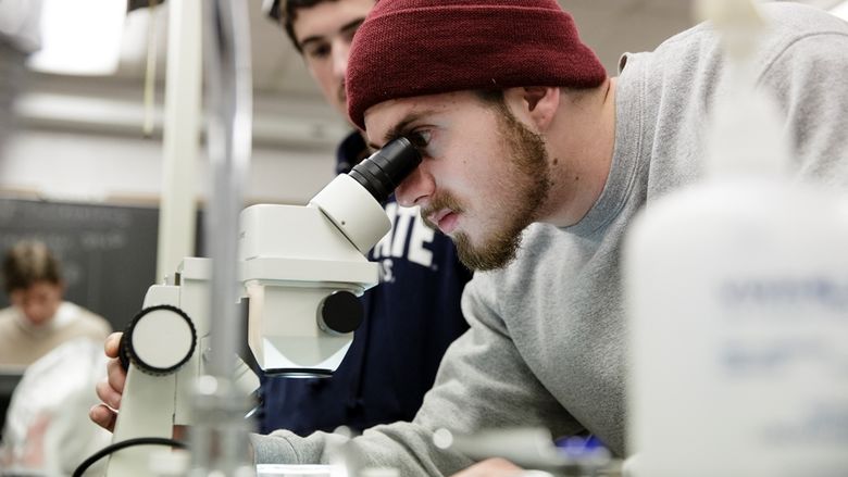 A student looking through a microscope in a classroom.