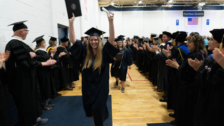 A female graduate with her arms in the air celebrates graduation. 