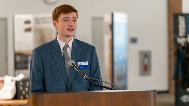 Student in a suit speaking from a wooden podium.