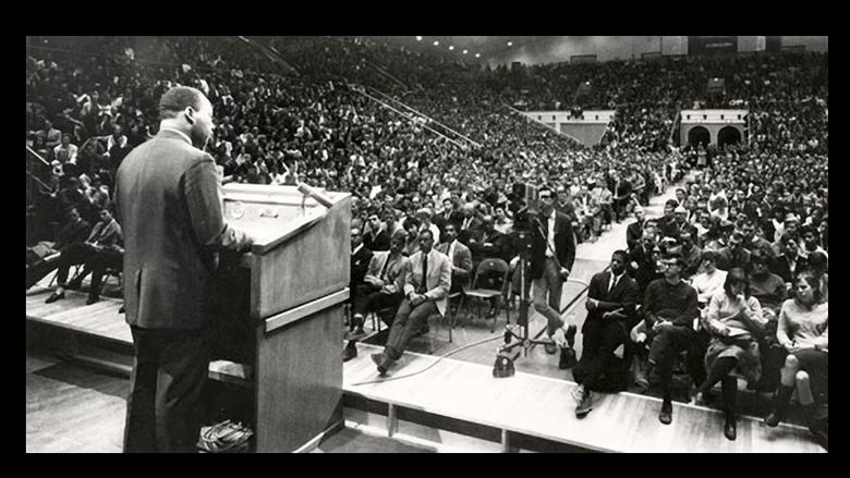 A black and white photo of Martin Luther King Jr. speaking at Rec Hall to a large audience
