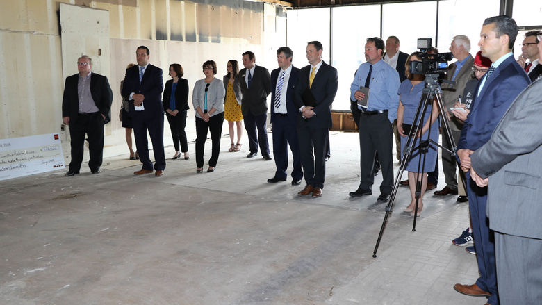 Group of people standing in a building undergoing renovation and watching a check presentation. 