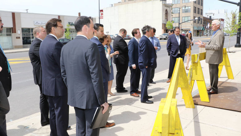 Man standing behind yellow construction barrier talking to a group of business people. 