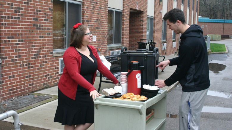 Associate Director of Student Services and Engagement Devon Purington serves coffee and danish to a student outside the residence halls at Penn State Hazleton.