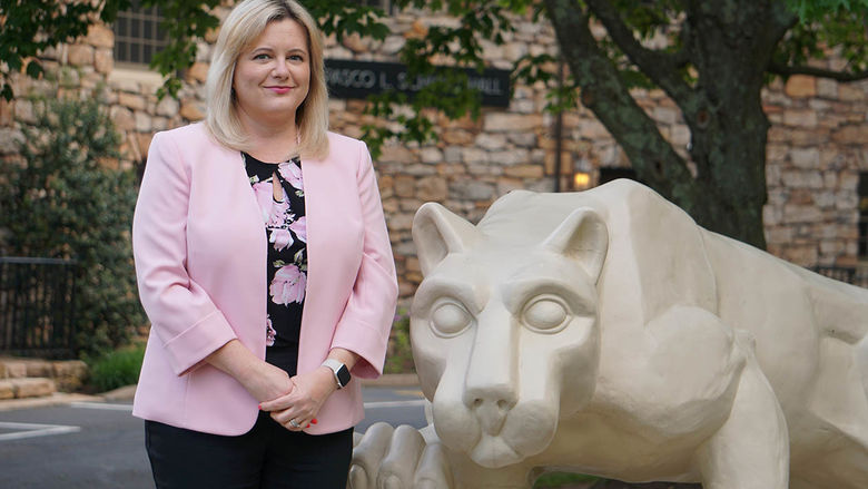 Woman in pink blazer standing next to statue of Nittany Lion.