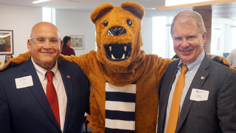 Two men posing for photo with arms around Nittany Lion mascot.