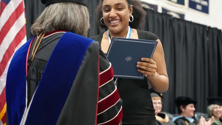 Student in black dress receiving certificate from chancellor.