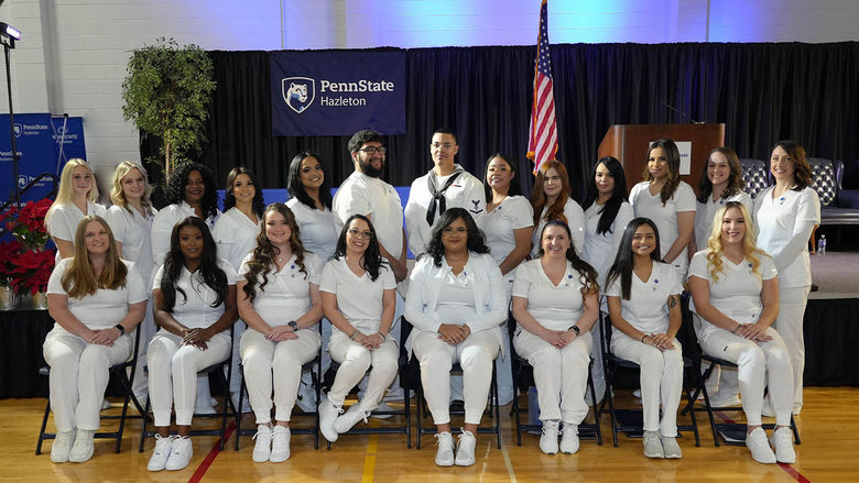 Male and female practical nursing students in white scrubs seated in two rows.