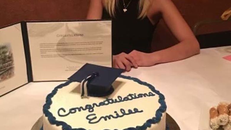 Woman in graduation cap sitting at a dinner table in front of a cake and her degree.
