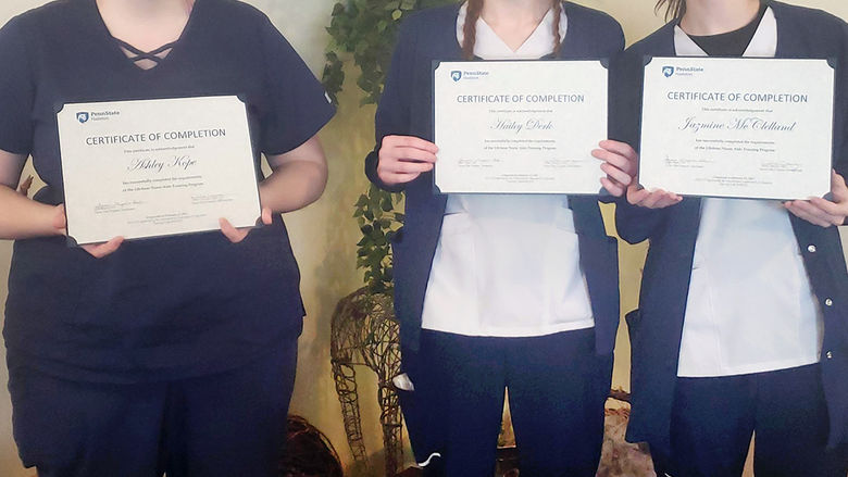 Three female students wearing masks and holding up certificates.