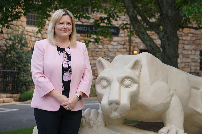 Woman in pink blazer standing next to statue of Nittany Lion.