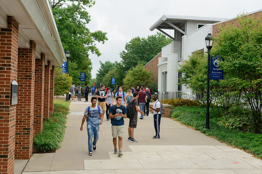 Crowd of students walking along a sidewalk on a college campus.