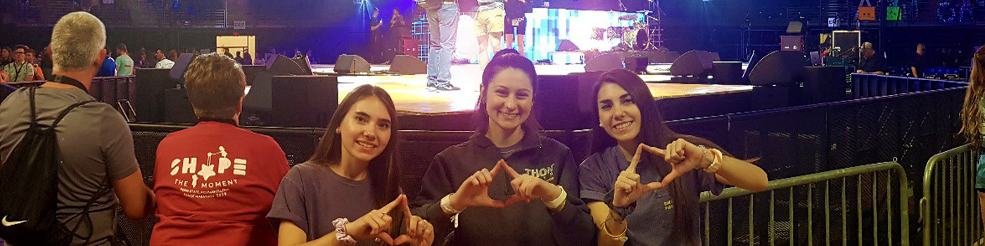 Students standing in front of stage at THON making diamond sign with their hands.