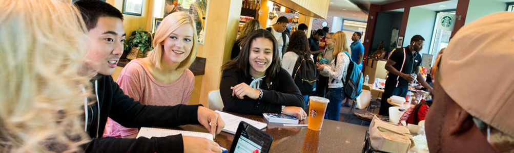 Students seated around a table in a cafe smiling and laughing.
