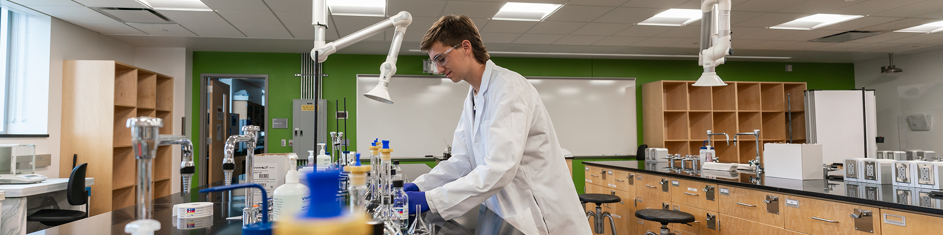 Male student in white lab coat handling laboratory equipment.