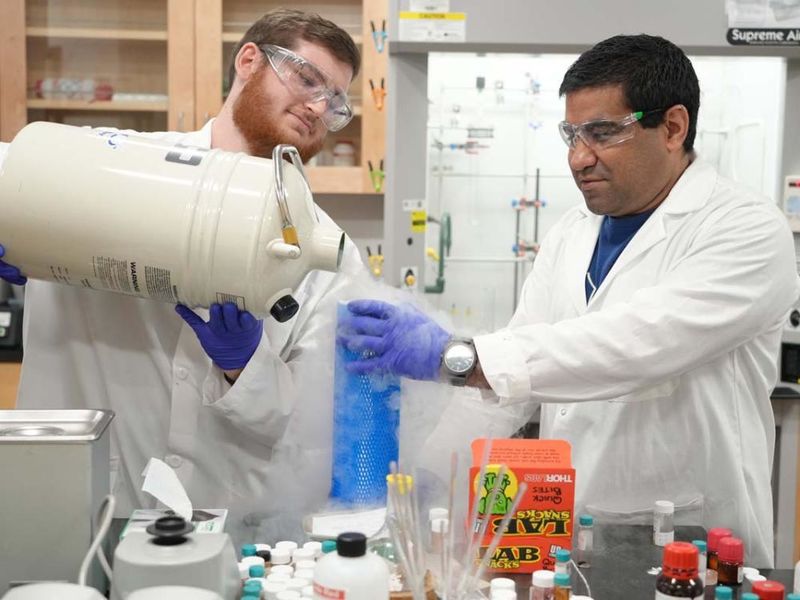 A student and professor in white lab coats pouring liquid nitrogen in a lab