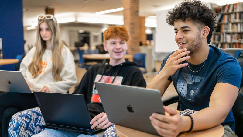 Three students seated and laughing in conversation with each other in a library.