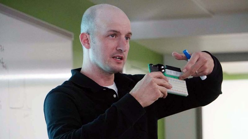 Professor pointing to a microchip board he is holding in his hands