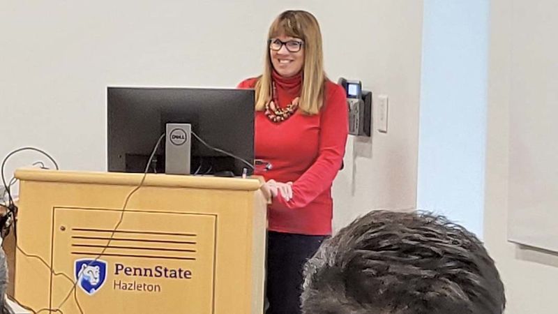 Female instructor standing behind wooden podium in front of classroom.