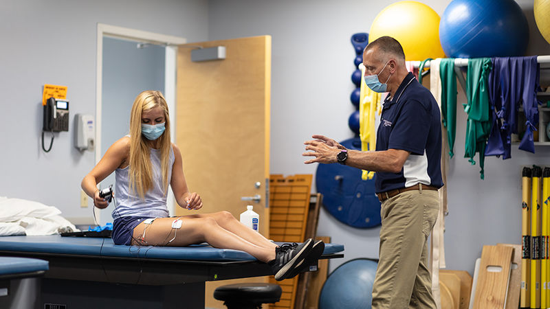 Instructor in classroom teaching physical therapy assistant student sitting on medical bed.
