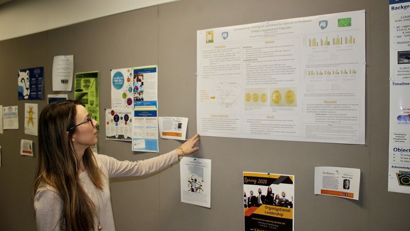 Professor in classroom pointing at scientific posters on wall