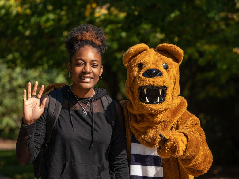 Female student in black hoodie waving next to Nittany Lion mascot.