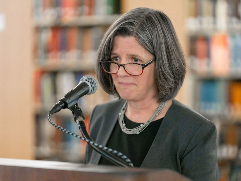 Woman with glasses speaking into a microphone at a podium.