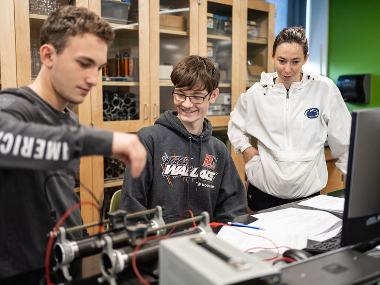 Three students in classroom lab working on physics equipment.