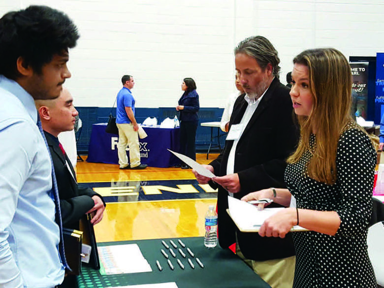 Two career services representatives providing information at a table across from two other people inside a gymnasium.