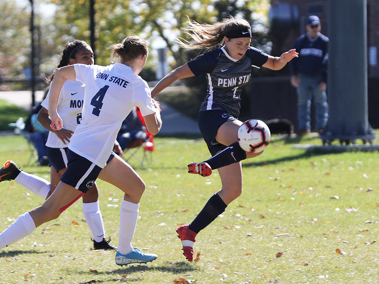 Female soccer player kicking soccer ball with two opponents in pursuit.