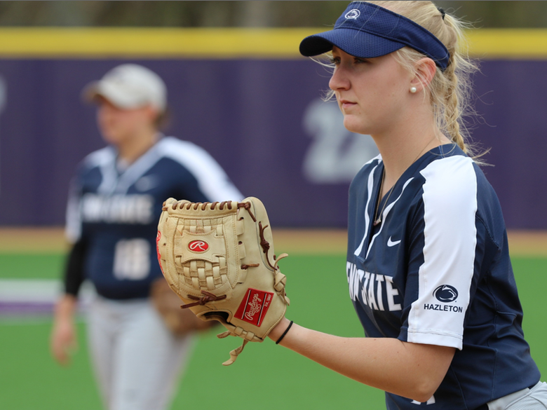 Softball pitcher holding glove and staring towards home plate with another female player in background.