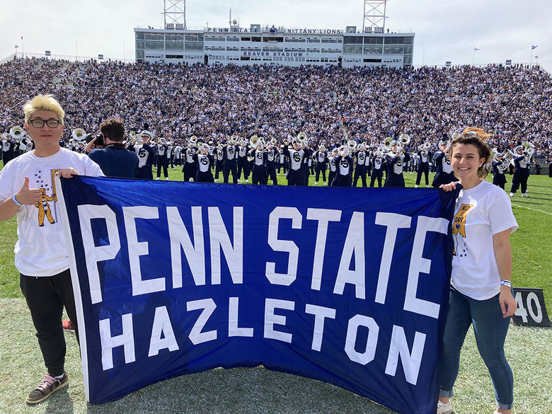 Students holding Penn State Hazleton banner on field of football stadium.