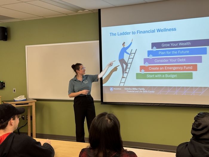 A student points to information on a screen while leading a presentation to a class