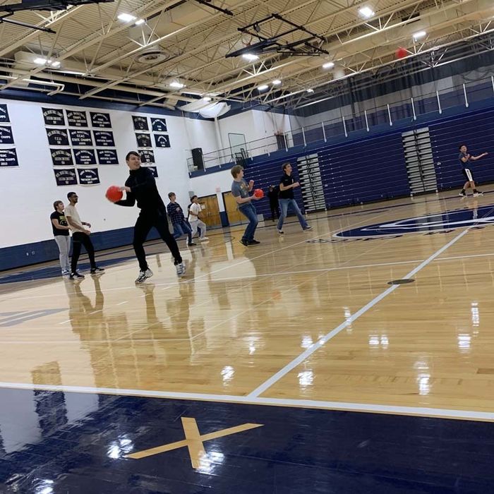 Students on a basketball court throwing dodgeballs.