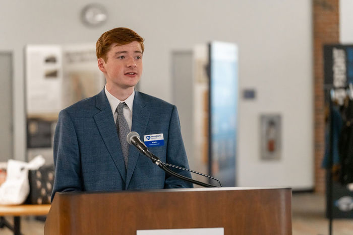 Male student in a light blue suit speaking from a podium.