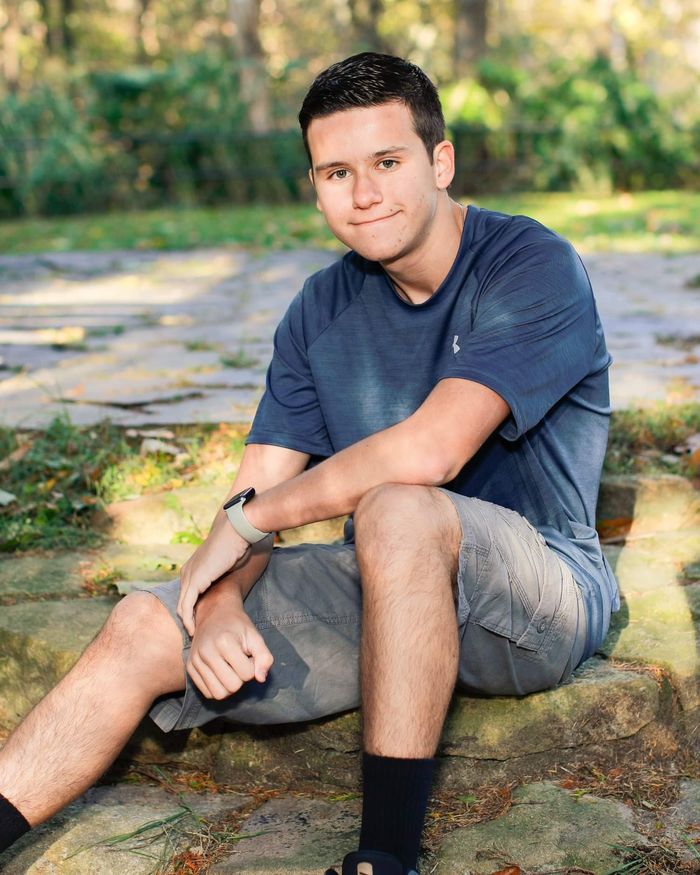 Male student in shorts and t-shirt sitting on a rock.