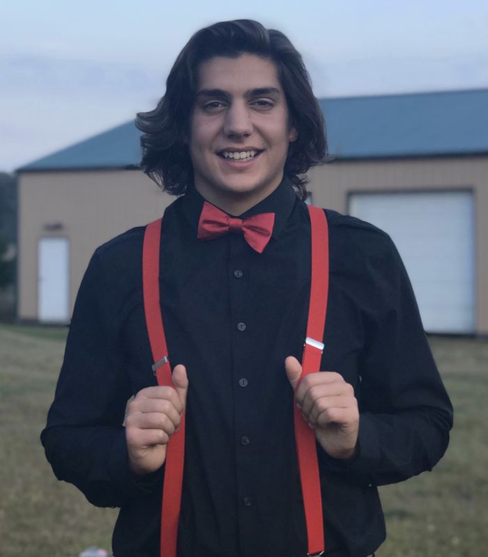 Student wearing a red bow tie with red suspenders over a black dress shirt posting outdoors.