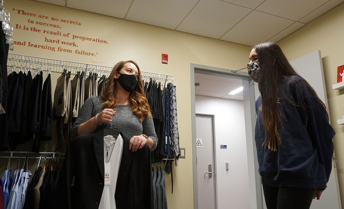 A student looks on as a staff member displays a professional outfit on a hanger.