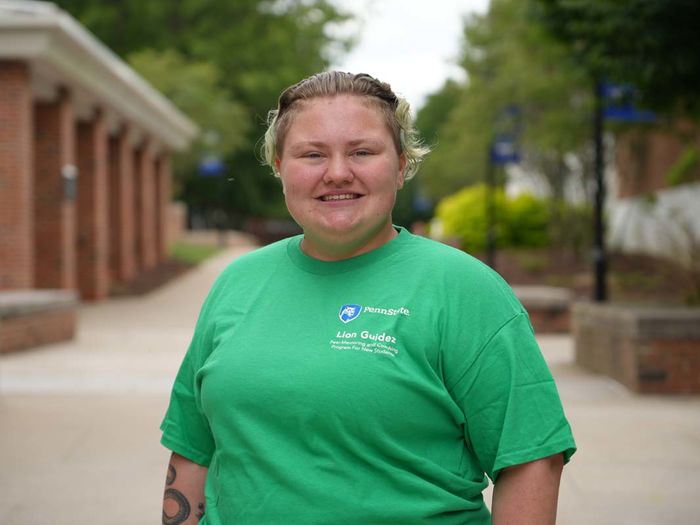 Student in green t-shirt standing on a sidewalk on a college campus
