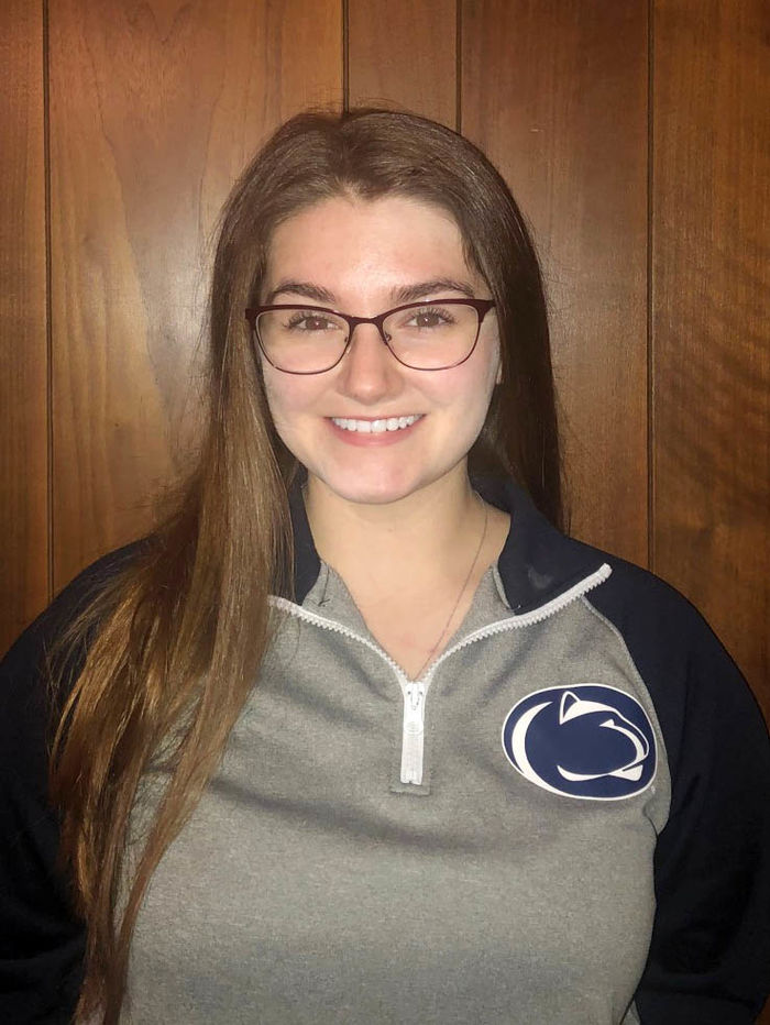Female student in front of brown wall wearing Penn State sweatshirt