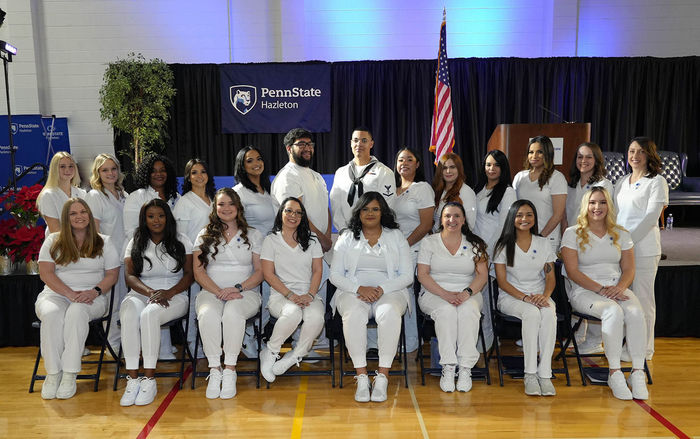 Male and female practical nursing students in white scrubs seated in two rows.