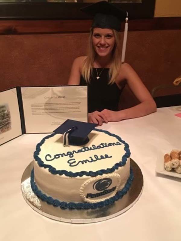 Woman in graduation cap sitting at a dinner table in front of a cake and her degree.