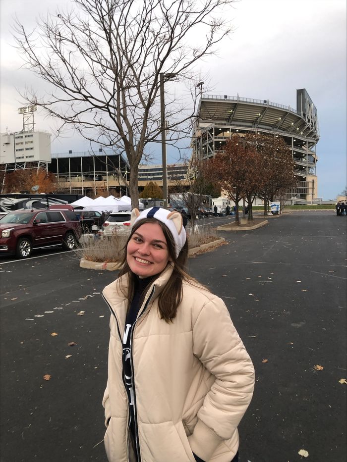 Woman in tan winter jacket standing in front of football stadium